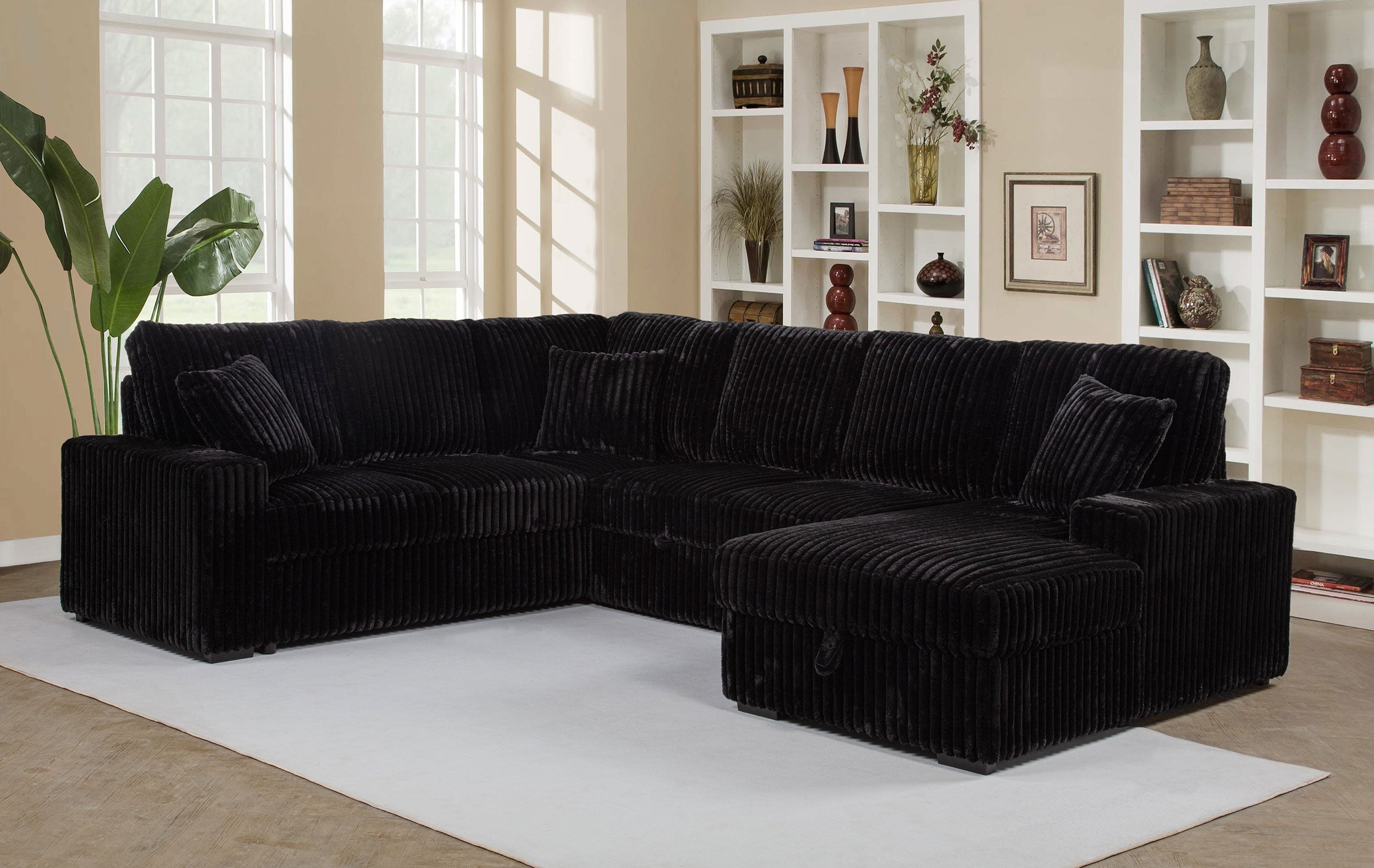 Black sectional sofa in a living room with bookshelves and decor.
