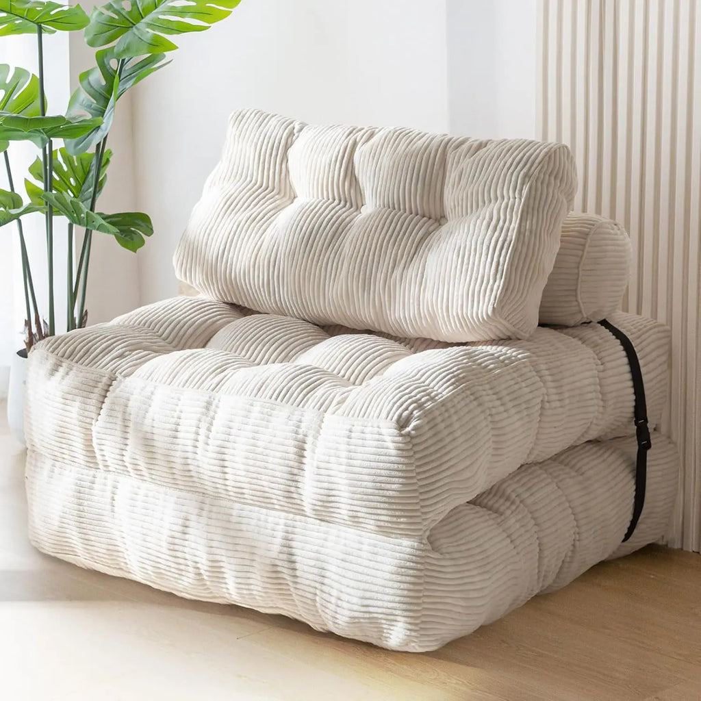 A cream-colored corduroy folding sofa bed with a matching back cushion, styled in a bright room with a wooden floor, a vertical slatted wall panel, and a potted green plant.