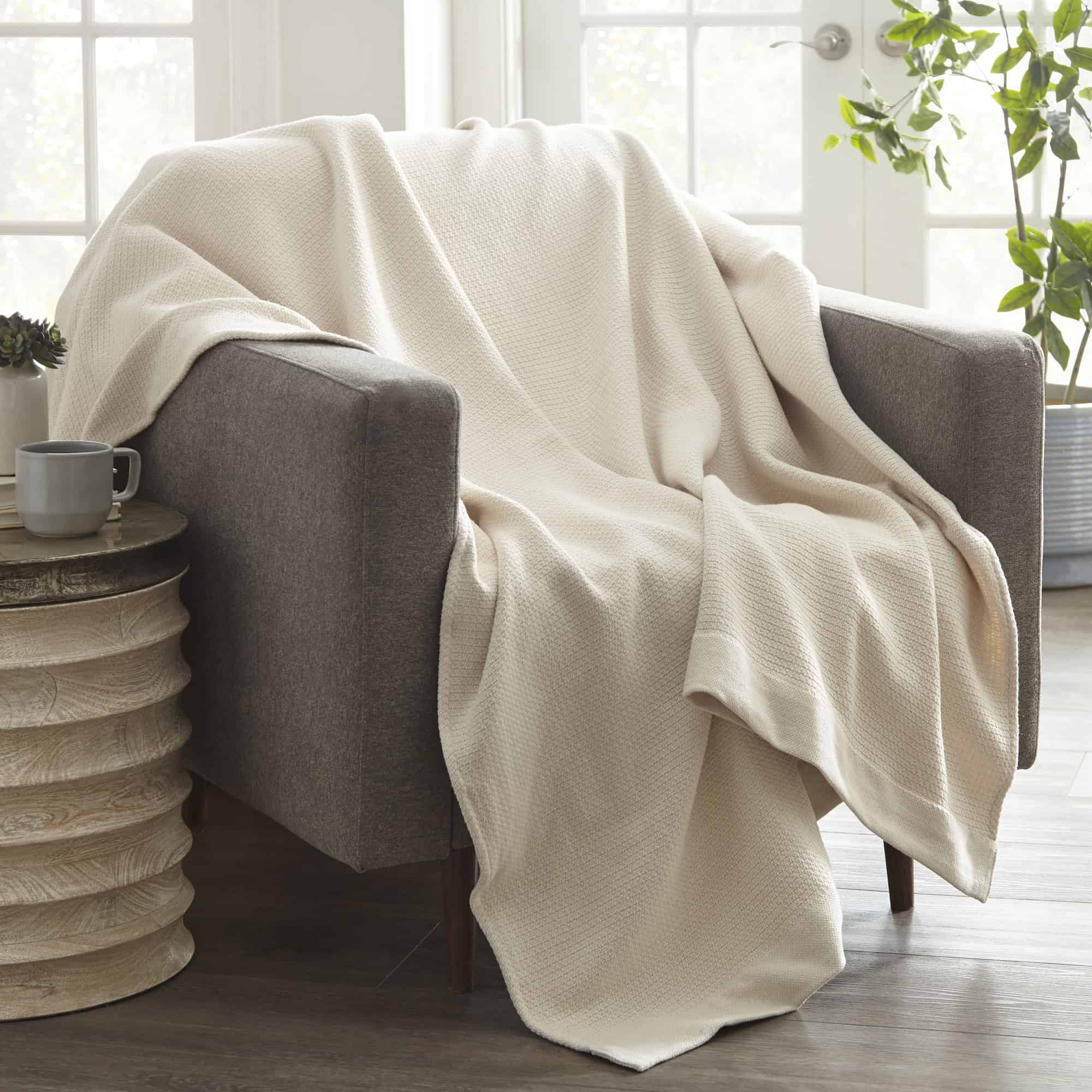 Beige blanket draped over a gray armchair in a bright room with a cup on a side table.